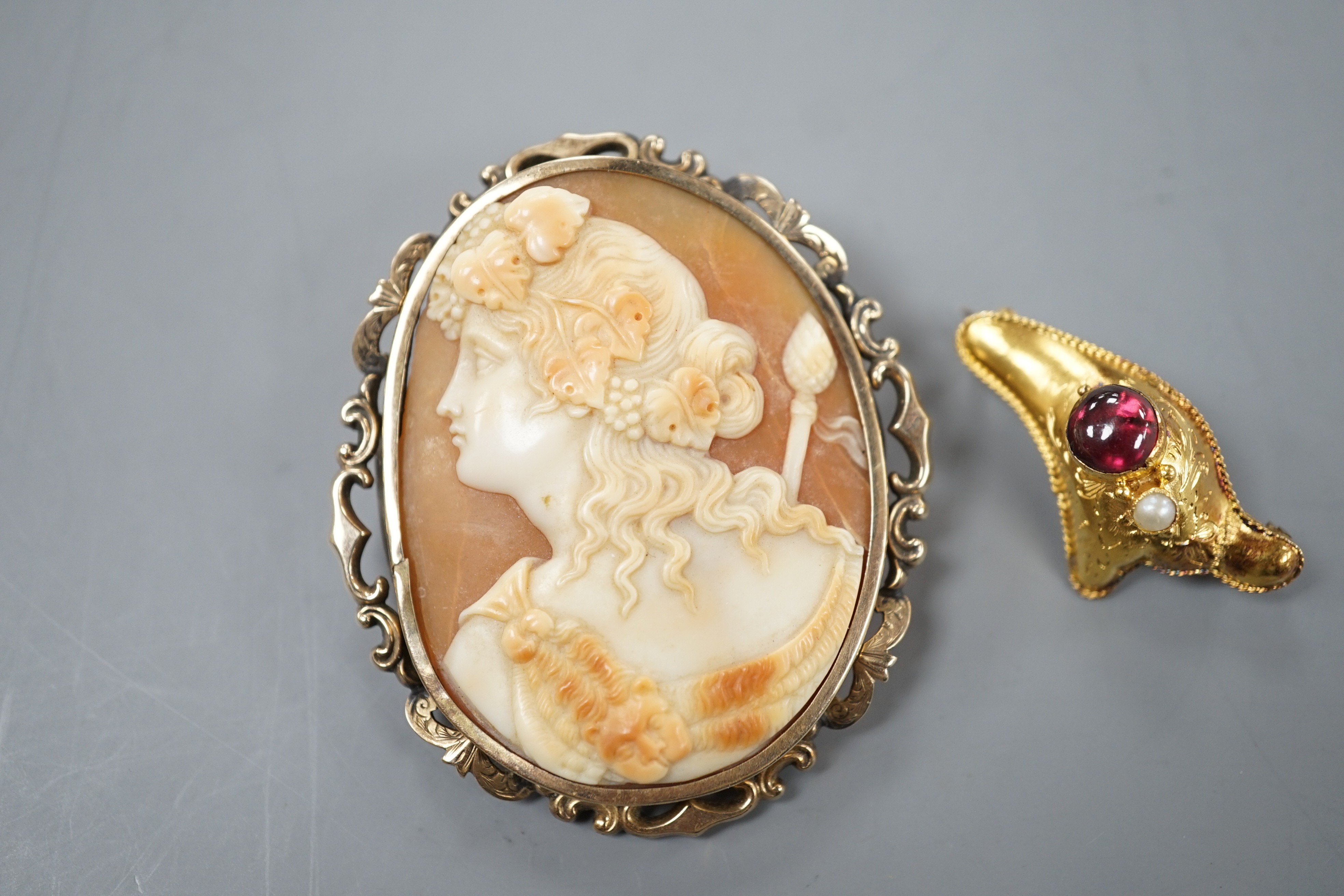 A yellow metal, garnet and seed pearl set brooch, 30mm gross 1.7 grams and a yellow metal mounted oval cameo shell brooch, 49mm, gross weight 10 grams.